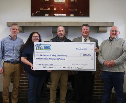 Five people holding a large check in an indoor setting with wooden paneling.