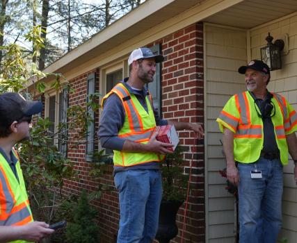 Three workers in yellow safety vests standing outside a brick building.