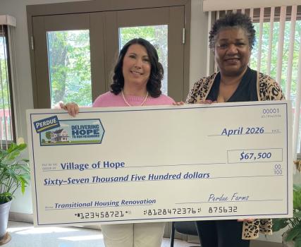 Two people holding a large check for Village of Ilion Community School District in a home interior.