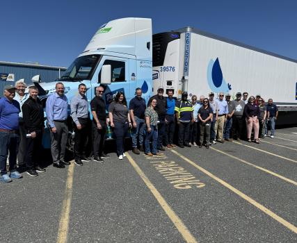 Group of people standing in front of a white commercial truck on pavement.