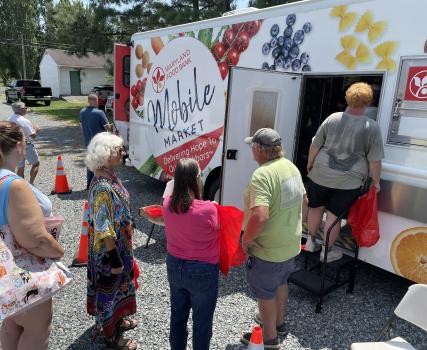 Group of people gathered at a food truck with colorful signage and hand-drawn artwork on the side.