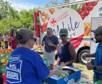 People in blue shirts gathered around a food truck at an outdoor event.
