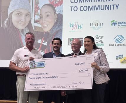Four people in white Perdue branded shirts holding oversized check at community event.