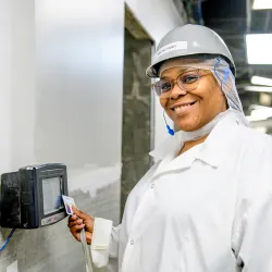 Person in white protective suit and face shield holding equipment in industrial facility