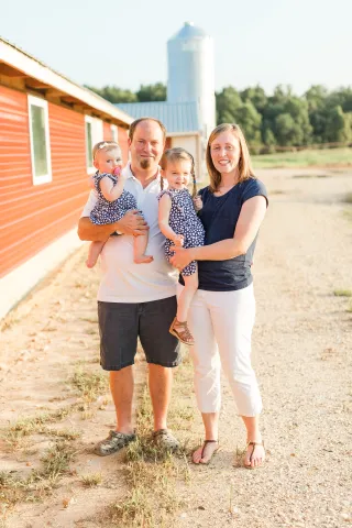 Three people standing outdoors in front of an orange building with a silo in the background.