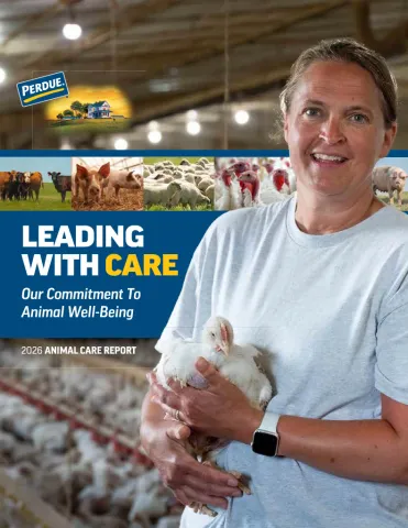 Man in white shirt holding chicken in poultry facility with "Leading with Care" text visible.