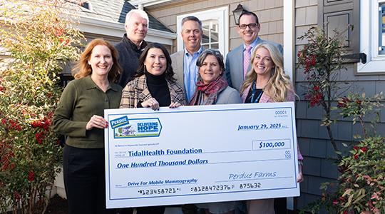 Group of people holding a large ceremonial check outdoors in front of a building.