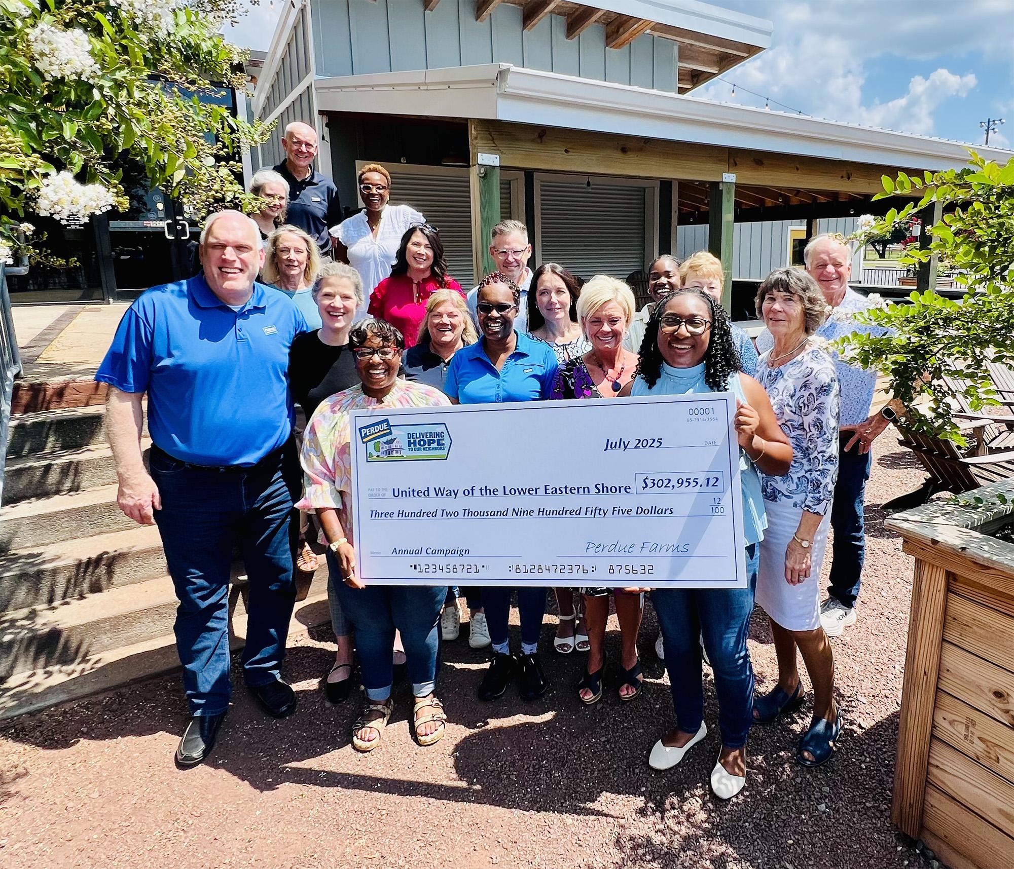 Group of people holding oversized check at outdoor Perdue facility setting.