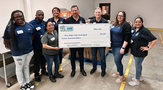 Group of people in blue Perdue apparel holding oversized check in indoor facility setting.