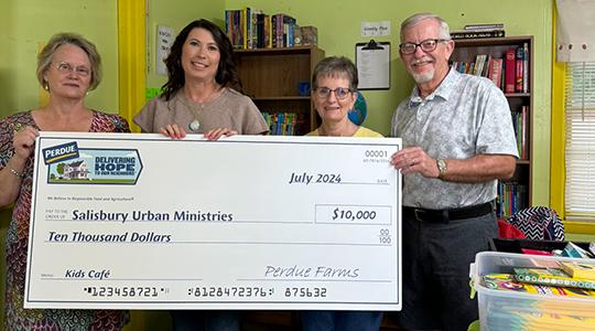 Four people holding large ceremonial check in front of bookshelf in yellow-green room.