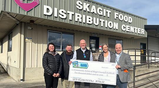 Group of people holding oversized check outside Skagit Food Distribution Center building.