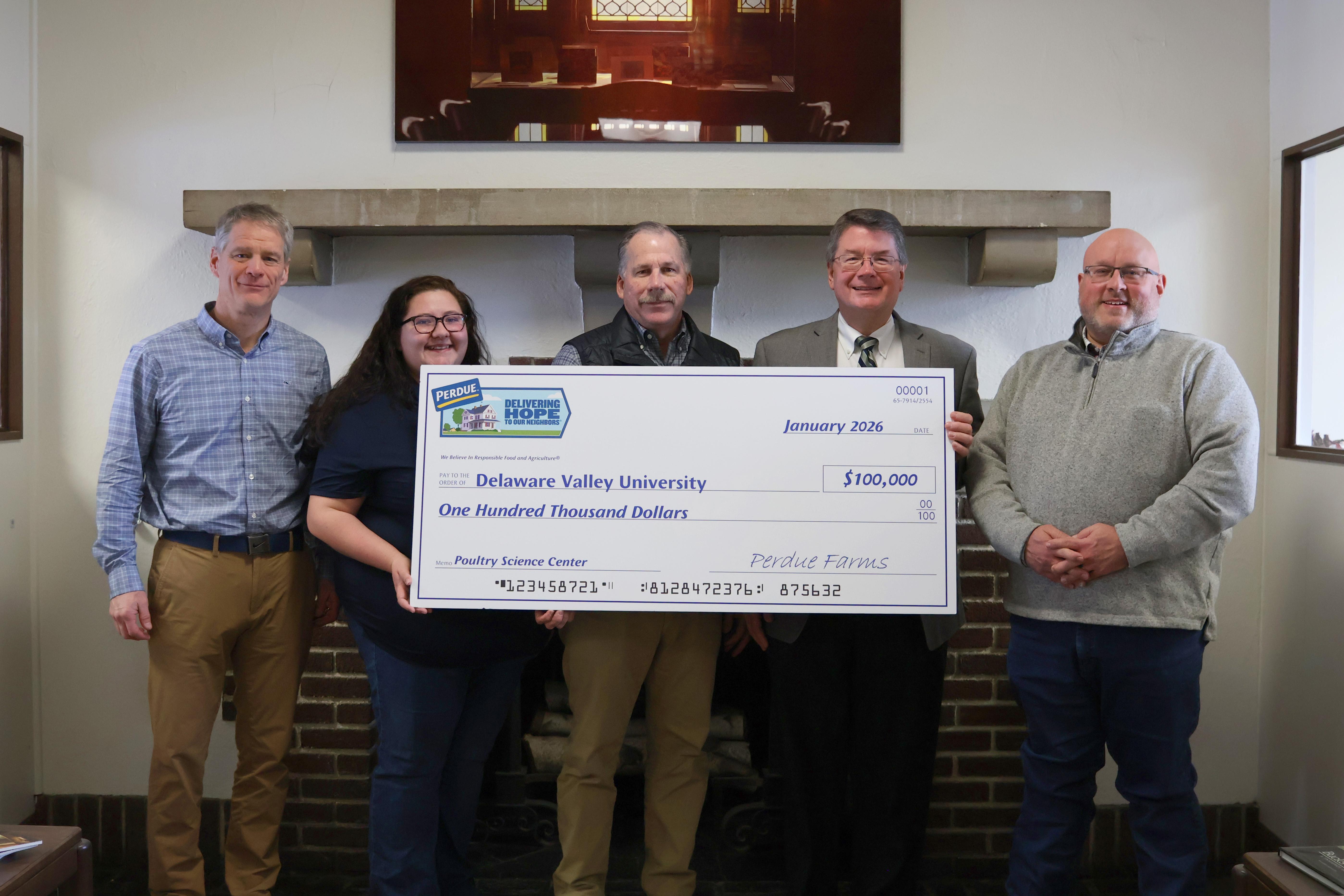 Five people holding a large check in an indoor setting with wooden paneling.