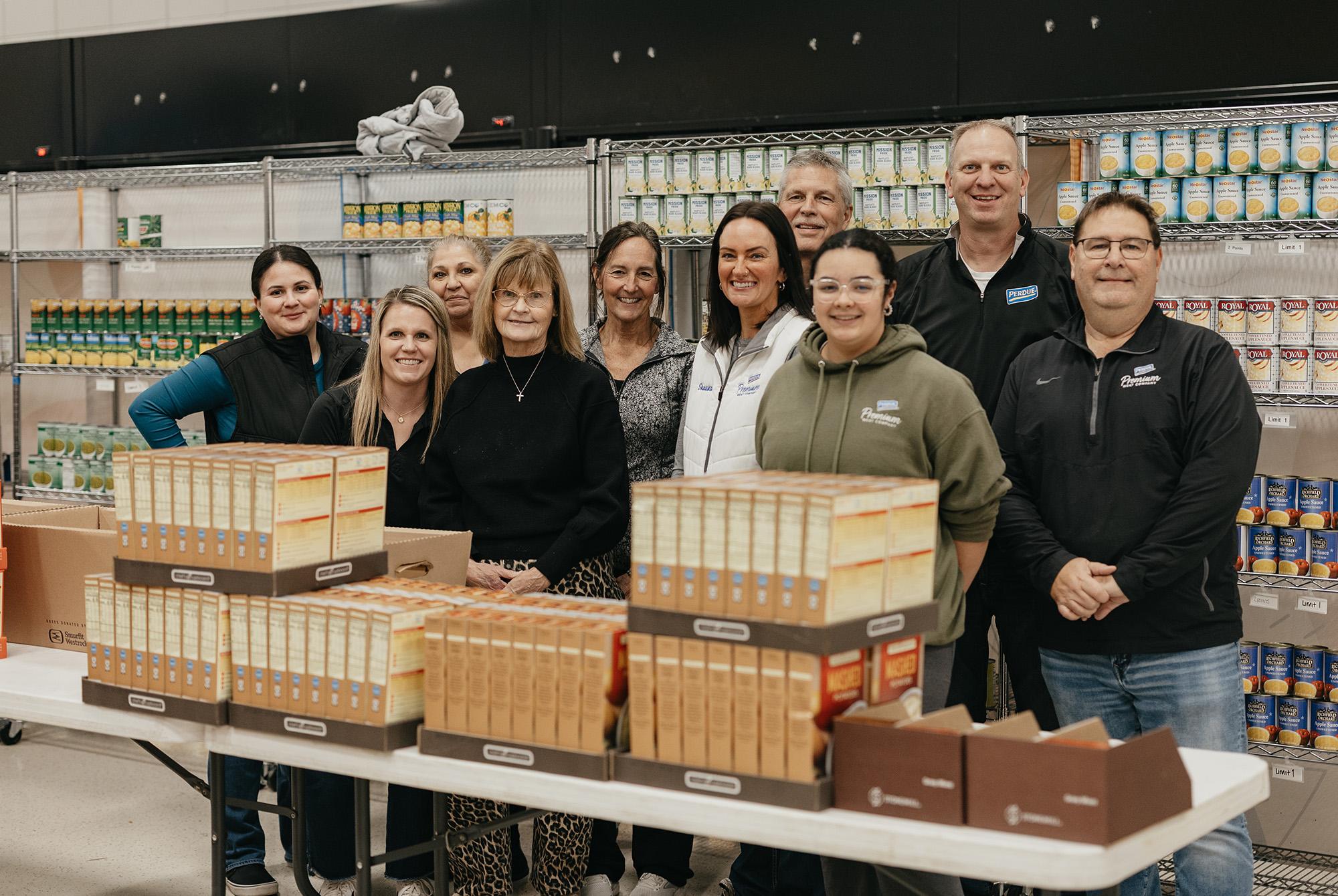 Group of people standing behind a table with stacked cardboard boxes in a Perdue facility setting.