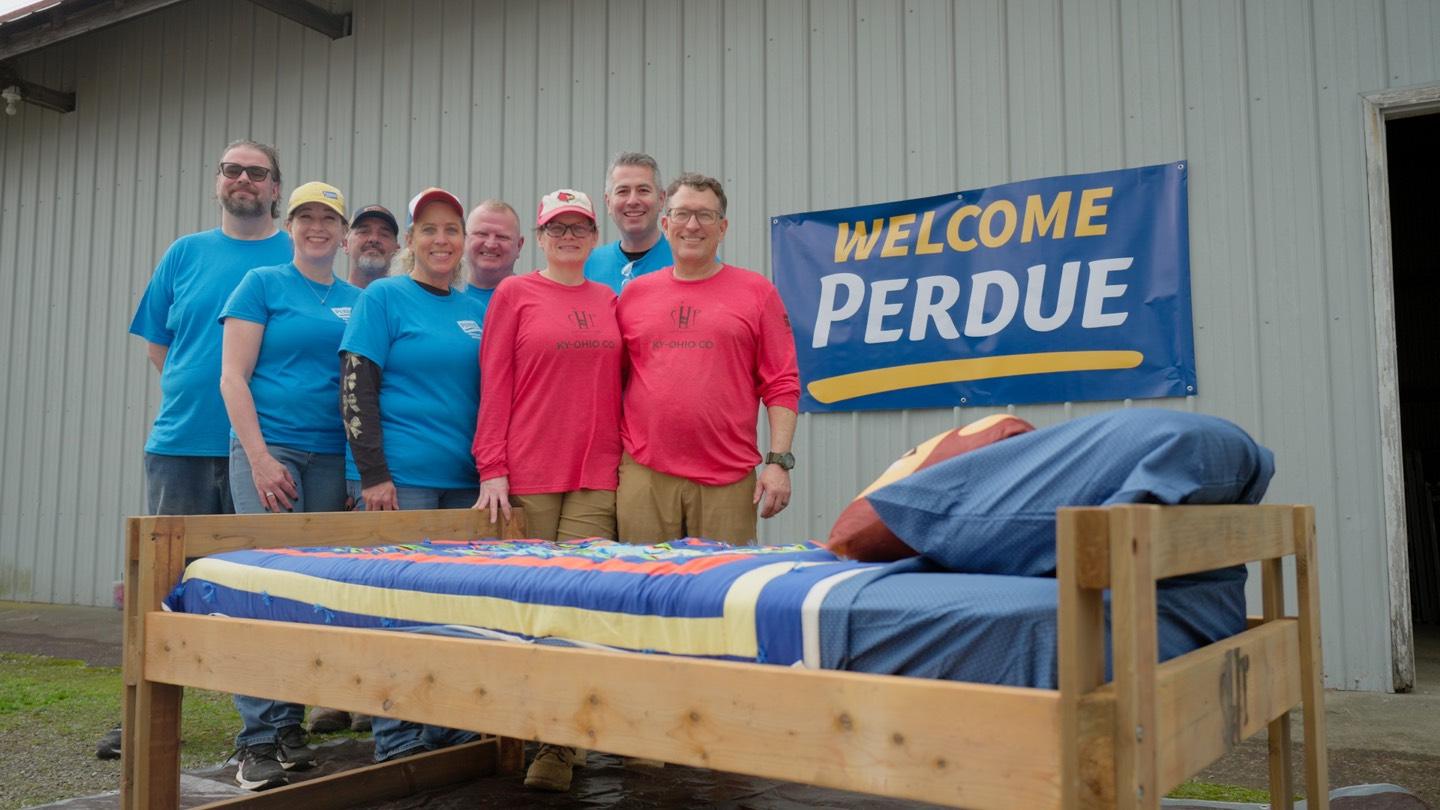 A group holding tools to build a bed as part of Perdue's charity initiatives.