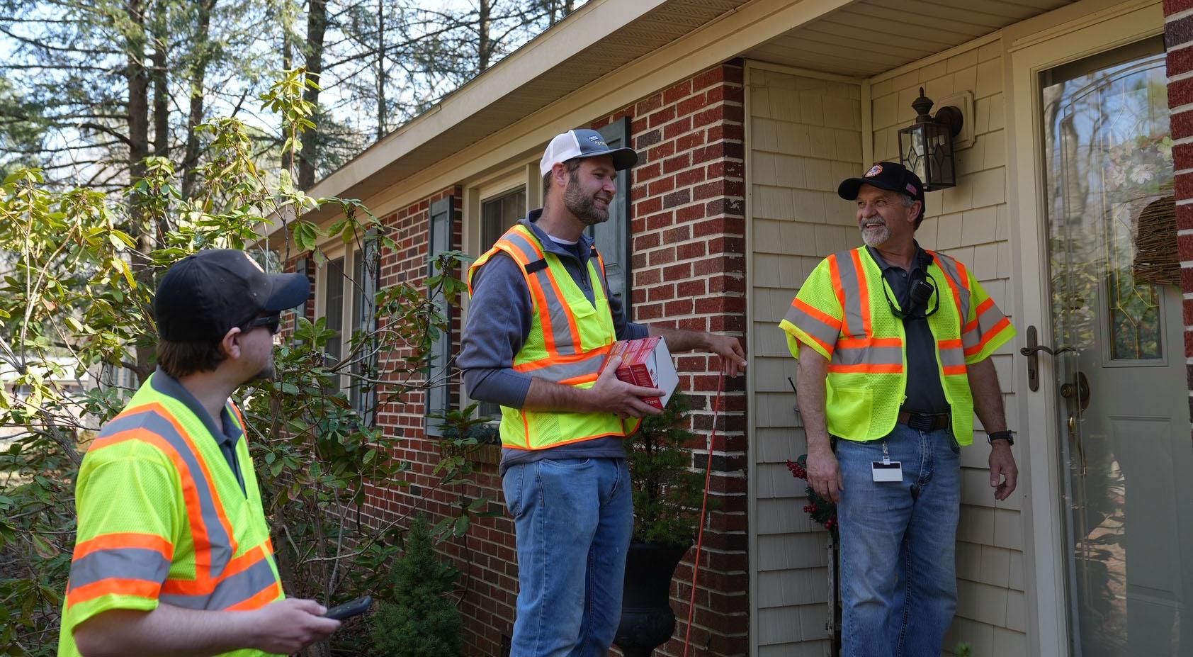 Three workers in yellow safety vests standing outside a brick building.