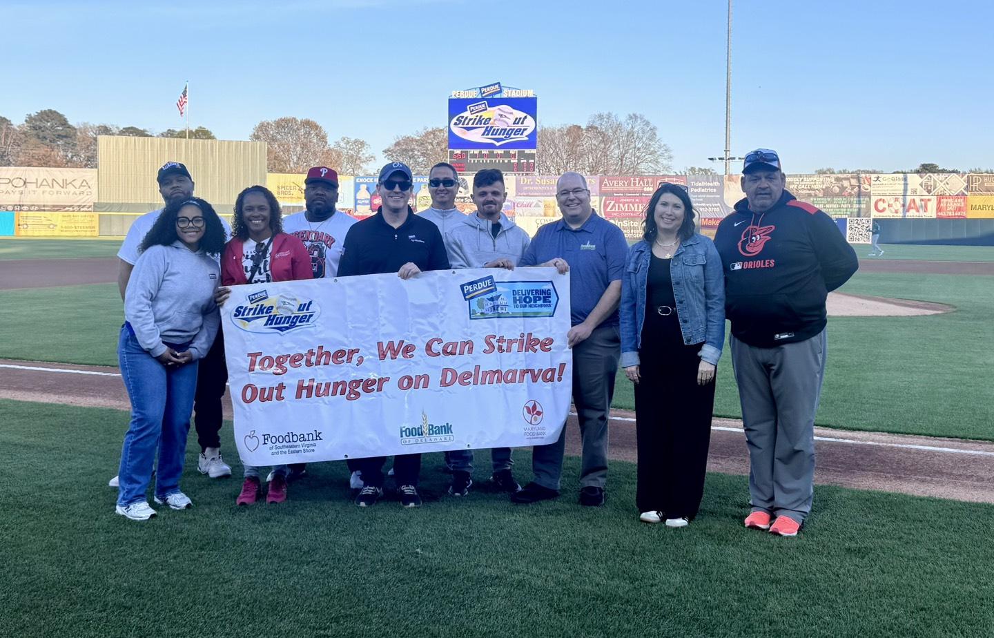 A group of people involved in the Perdue Strike Out Hunger 2026 campaign, holding a banner that says "Together, We Can Strike out Hunger on Delmarva!"