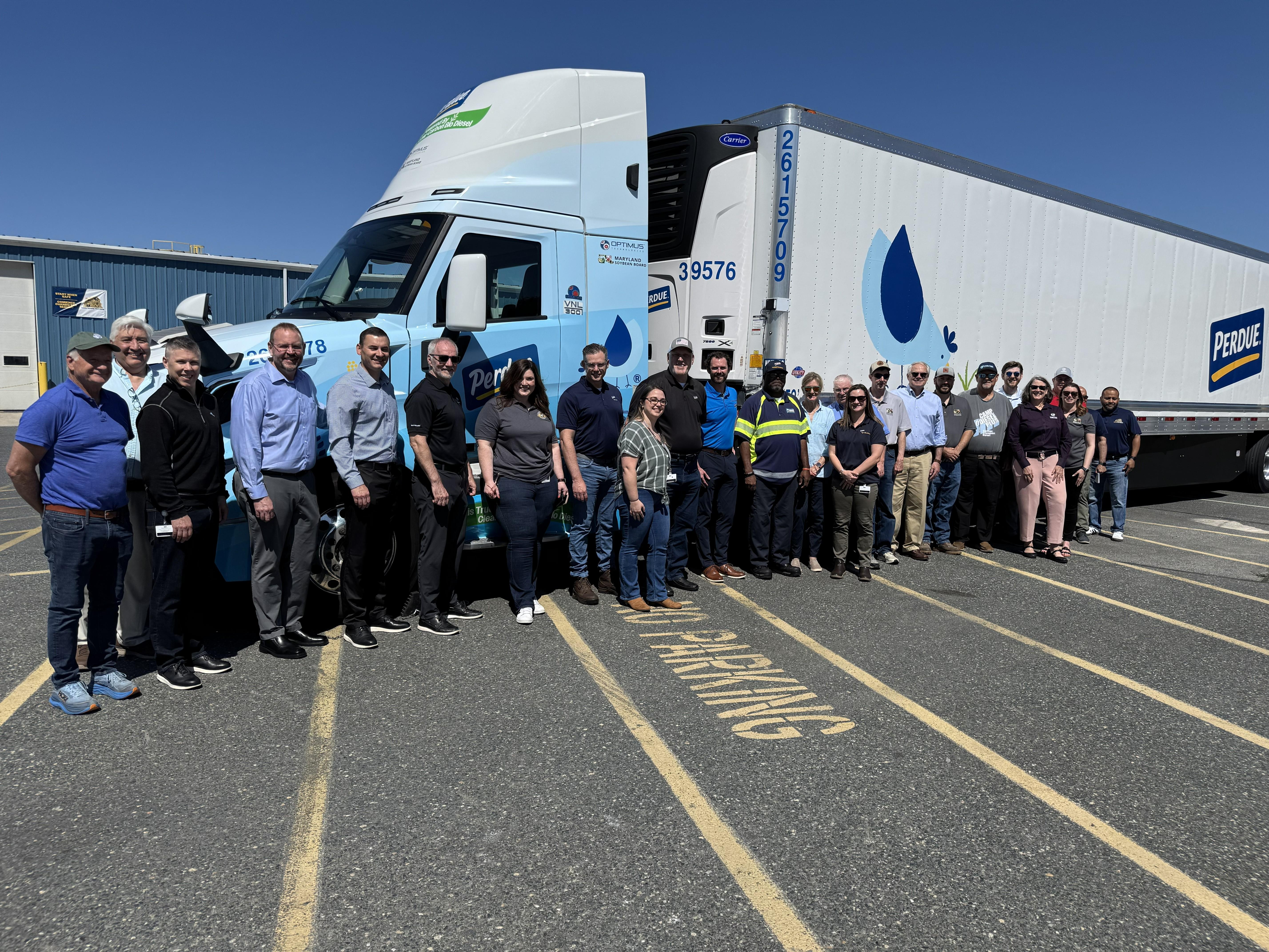 Group of people standing in front of a white commercial truck on pavement.