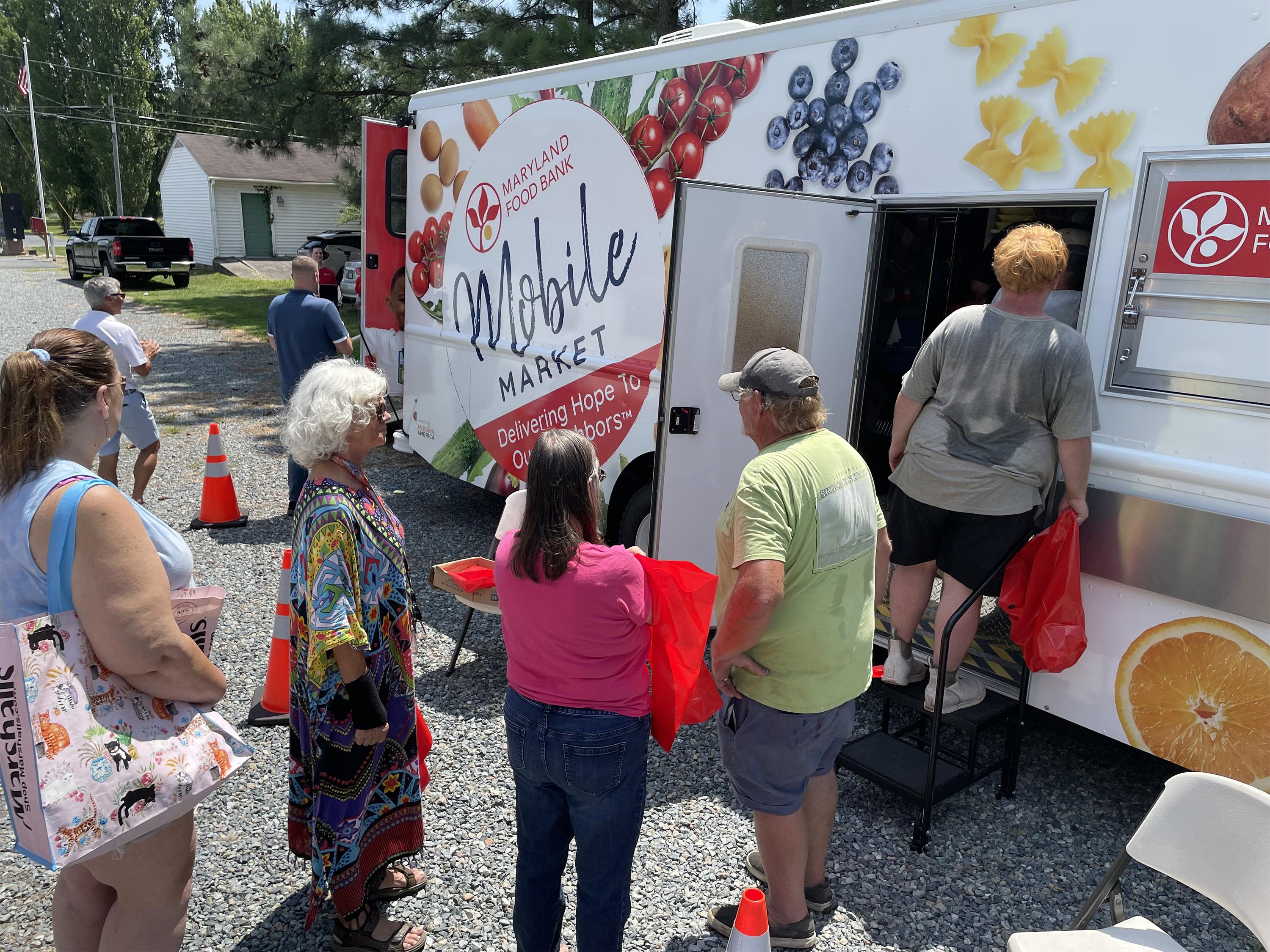 Group of people gathered at a food truck with colorful signage and hand-drawn artwork on the side.