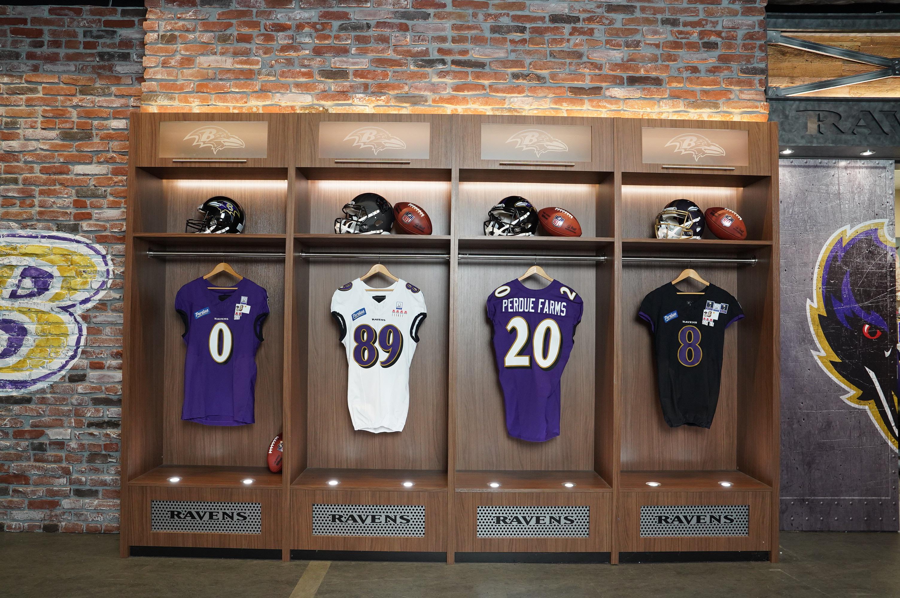 Four Perdue-branded sports jerseys displayed in illuminated cases against a brick wall.