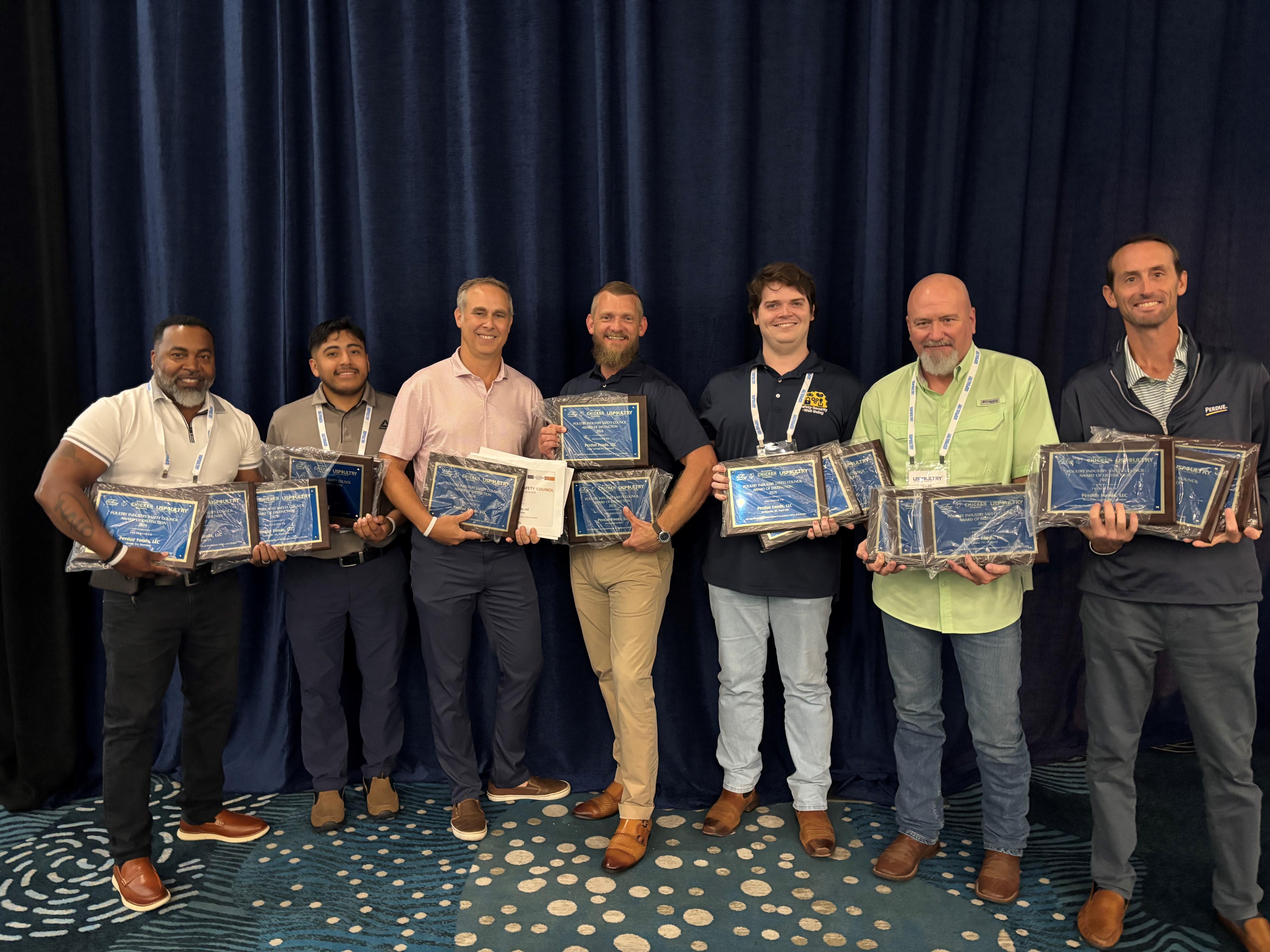 Six people standing in a line holding certificates in front of a dark blue curtain.