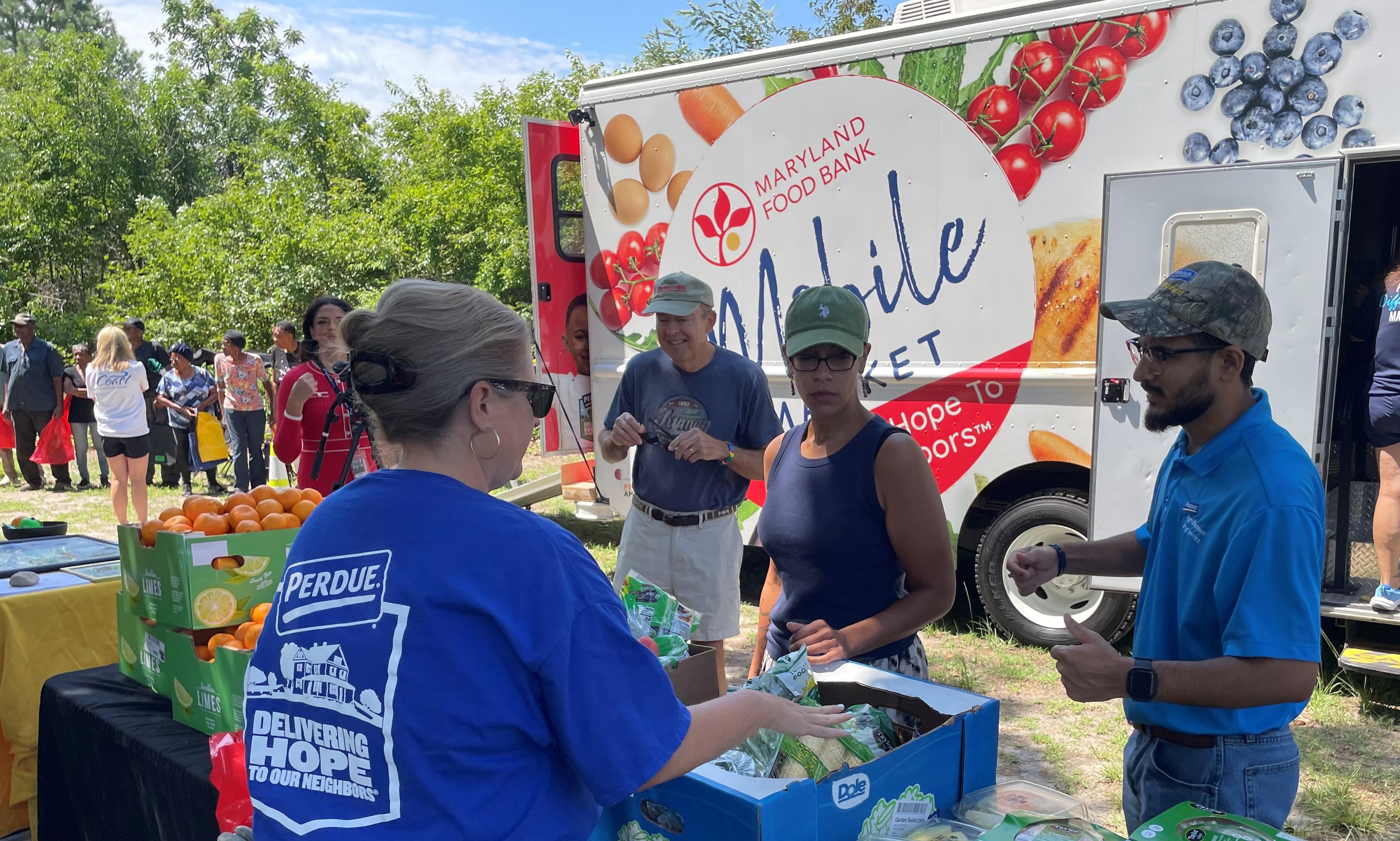 People in blue shirts gathered around a food truck at an outdoor event.