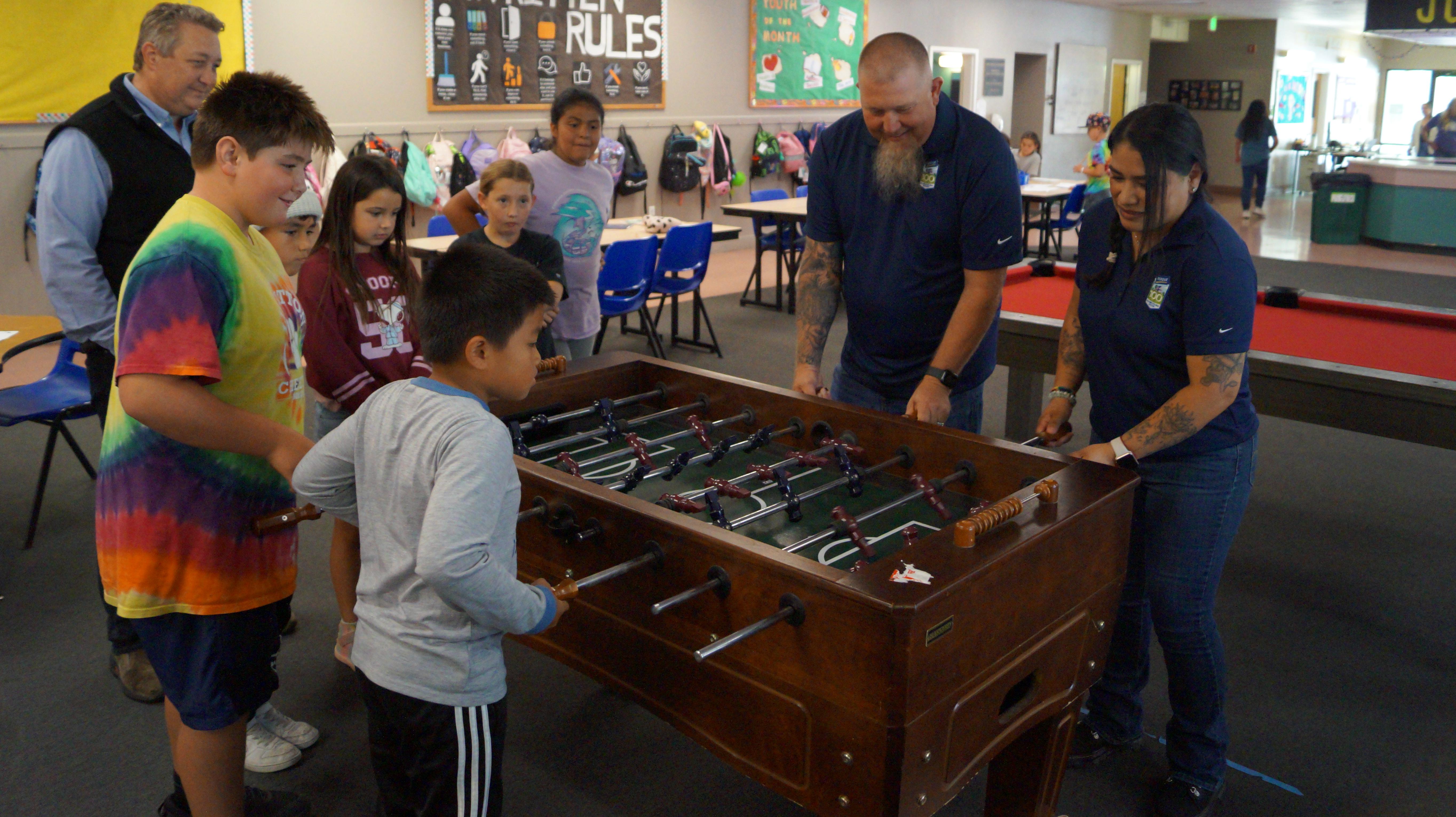 Group of people playing foosball in a recreational facility with colorful striped wall decoration.
